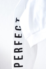 Closeup of folded snow white youth sweater fabric with word Perfect on sleeve. Clear white clothes concept