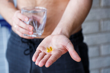 A young man holds vitamins and a glass of water in his hands. Immunity pills