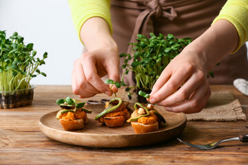 Woman putting fresh micro green on tasty sandwiches