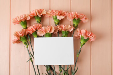 Obraz premium Fresh carnation flowers with empty paper sheet on color wooden background