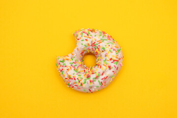 Fototapeta na wymiar Donut with colorful sprinkles on yellow background. Pink frosted donut with colorful sprinkles.