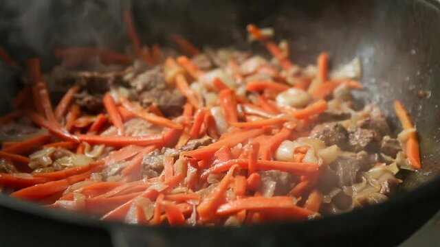 Meat, carrot and onions are stewed in a cauldron in a sauce close-up.The cook covers the ingredients with a lid. Cooking pilaf in a cast-iron kazan, zirvak, oriental cuisine. Step 7 of 8