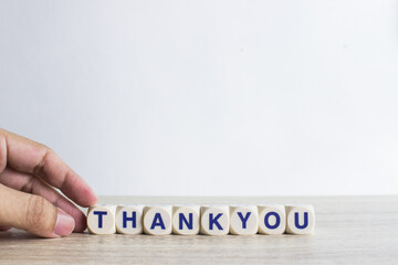 A word " Thank you" on a wooden table over a light background. 