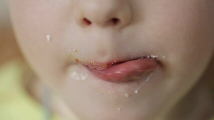 A little caucasian girl licks her lips and mouth with her tongue after sweets. Child with a sweet tooth, close-up