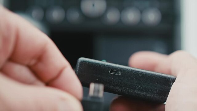 Focused view of black electronic device with mini USB port. Close up of man hand plugging mini USB into port.