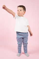 Happy little kid imitate superhero. Boy in a superman pose on pink background