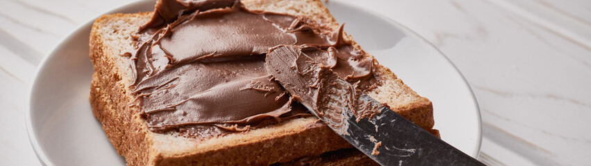 Slices of bread with chocolate hazelnut cream and knife on a wooden background panorama