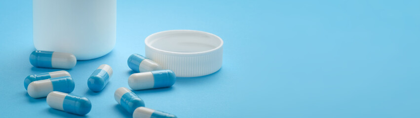 Container and capsules on blue background with copy space banner
