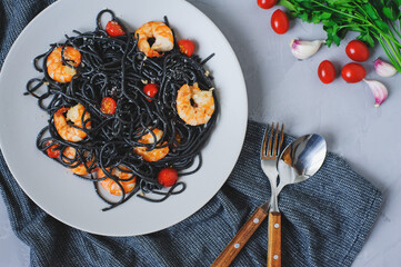 black spaghetti pasta with cherry tomatoes and shrimps served in plate. Tasty vegetarian italian food