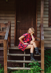 happy woman sitting on porch of her wooden country house. Rural living, running away to nature, ecology concept
