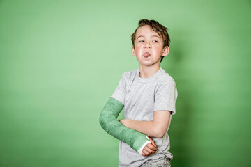 cool young schoolboy with broken arm and green plaster posing in front of green background in the studio