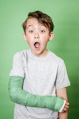 cool young schoolboy with broken arm and green plaster posing in front of green background in the studio