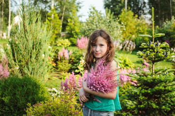 happy kid girl picking bouquet of astilbe flowers in summer garden