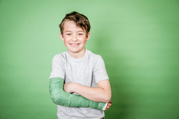 cool young schoolboy with broken arm and green plaster posing in front of green background in the studio