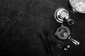 Steel bar tools and accessories for making cocktail. Shaker, jigger, strainer, spoon, tongs, muddler. Alcohol drink and beverages preparation concept. Black background, top view, copy space