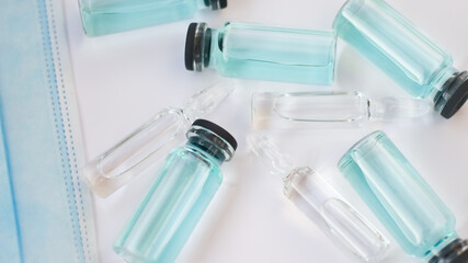 Vial vaccine, top view of glass ampoules with transparent and blue liquid lying on white background, global vaccination concept