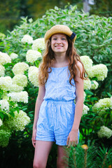 happy kid girl walking in blooming summer garden, posing near white hydrangea paniculata bush