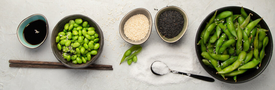Raw edamame soya beans with salt and sauce on light gray background.
