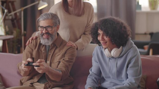 Beautiful woman smiling and embracing cheerful husband and son while they playing video game on console at home