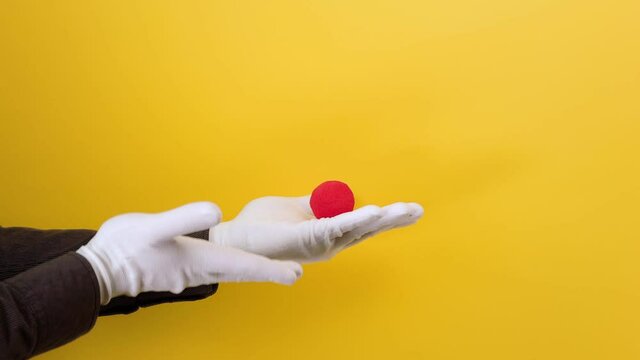 Male magician's hands in white gloves show the trick with a red foam ball. Yellow background. The concept of entertainment and illusions.