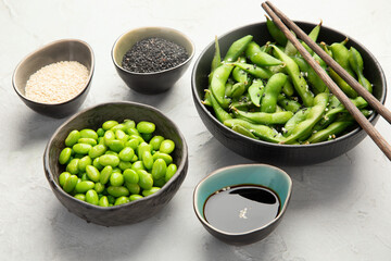 Raw edamame soya beans with salt and sauce on light gray background.