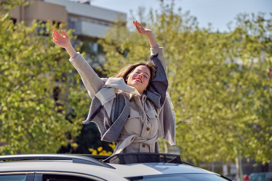 Joyful woman standing with arms raised in car sunroof