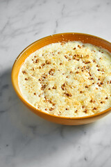 Buckwheat porridge cooked on milk in a bright yellow bowl on a light marble background