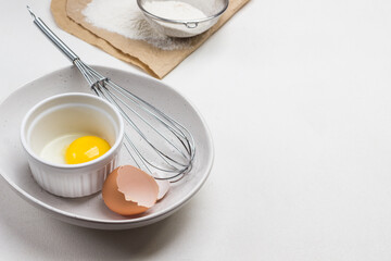 Eggshell, egg and whisk in bowl. Egg yolk in bowl. Flour and sieve on paper.