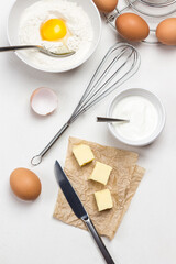 Whisk on table. Knife and butter on paper.