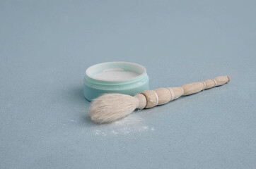Close-up cosmetics brush and powder on a blue background