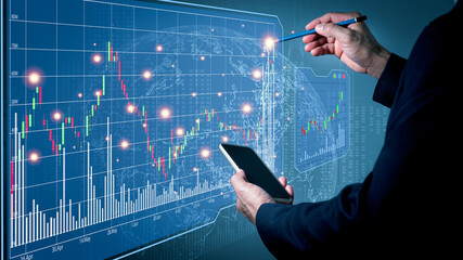 A man wearing a suit on his left hand holding a cell phone His right hand poked a pencil on a simulation fast-growing stock chart. Globe background and blurred lights