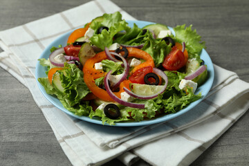 Plate of Greek salad and kitchen towel on gray textured background