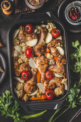 Tasty chicken drumsticks with vegetables  in cast iron pan on dark rustic background with fresh herbs. Healthy dieting food. Top  view. Chicken casserole