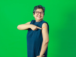 Adult senior Asian woman pointing and smile confident show shoulder with bandage plaster after getting Coronavirus of Covid-19 vaccine injection. Idea for vaccination of population against virus.