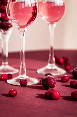 red berries scattering on the table among glasses with pink alcohol drink, ripe icing cherry among frozen cranberries closeup, elegant minimalism