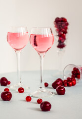two glasses of pink gin or vodka infused with cranberry on light background, berry liquor or any alcohol cocktail among red berries, minimalism