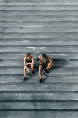 Fototapeta na wymiar Athletic couple sitting on concrete staircase after jogging or fitness workout outdoors