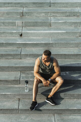 Confident athletic man sitting on concrete stairs after fitness workout outdoors