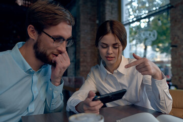 business man and woman sitting at a table in a cafe and looking at the phone
