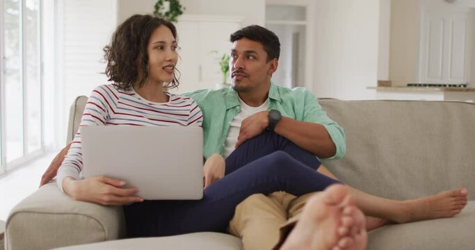 Hispanic couple sitting on sofa looking at laptop discussing