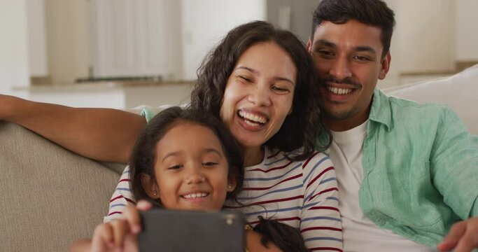 Happy hispanic parents and daughter sitting on sofa taking selfie