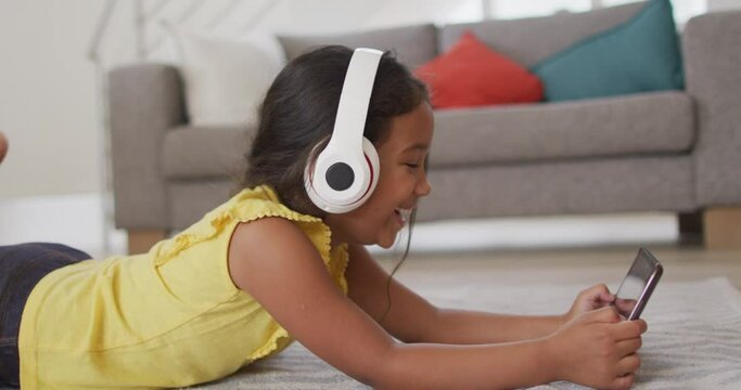 Happy hispanic girl watching video on tablet wearing head phones lying on floor