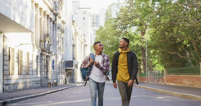 Two happy mixed race male friends walking and talking with backpacks