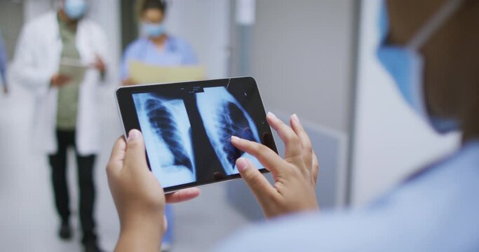 Mixed Race Doctor Wearing Face Mask Looking At X Ray On Tablet Walking In Hospital Corridor