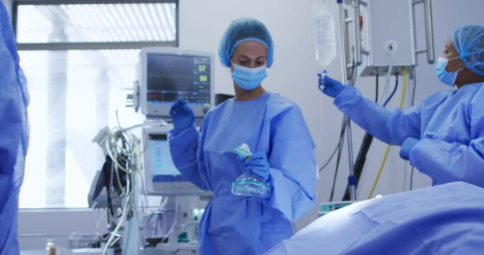 Diverse female surgeons wearing face masks and protective clothing during operation in hospital