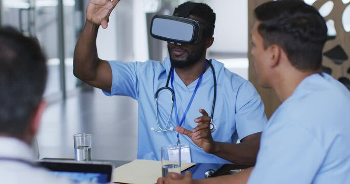African american male doctor at table using vr headset with a diverse group of colleagues watching