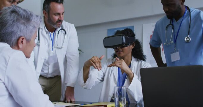 Asian Female Doctor At Table Using Vr Headset With A Diverse Group Of Colleagues Gathered Around Her