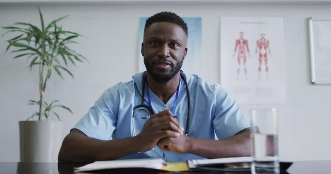 African american male doctor at desk talking and gesturing during video call consultation