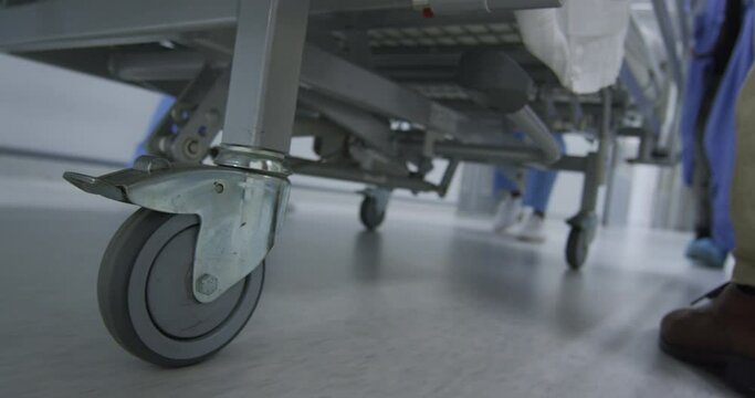 Feet of doctors walking through corridor transporting patient in bed on wheels