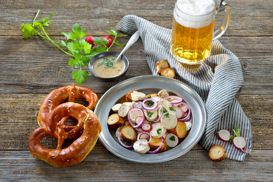 Bayerischer Wei&szlig;wurstsalat mit ger&ouml;steten Brezenscheiben auf Zinnteller dazu ein helles Bier &ndash; Delicious Bavarian salad with cut veal sausages and roasted pretzel slices with a mug of lager beer 